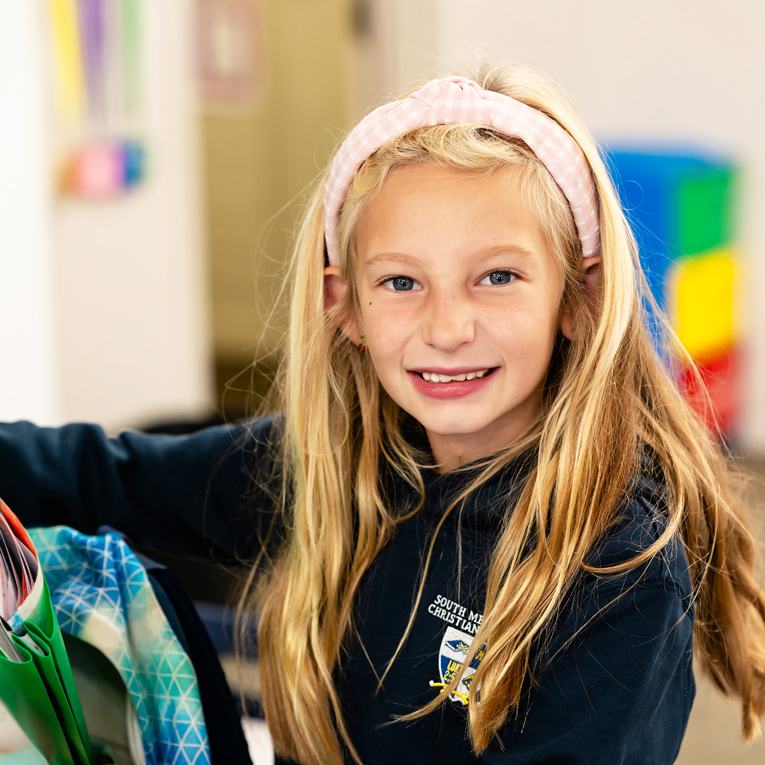 Elementary student smiles at the camera as she packs her backpack