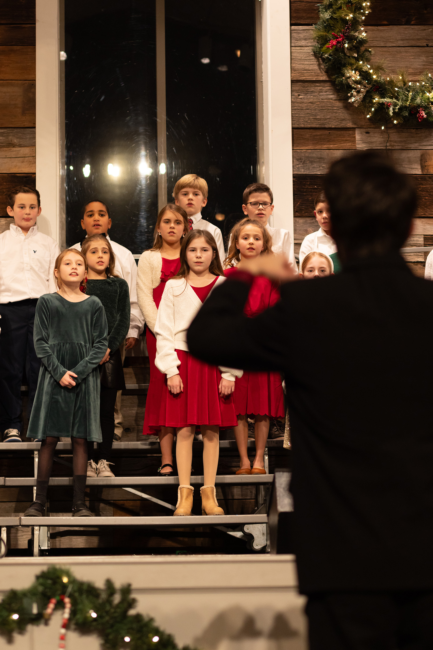 Group of elementary students dressed in Christmas outfits stand on risers performing at the Christmas Concert