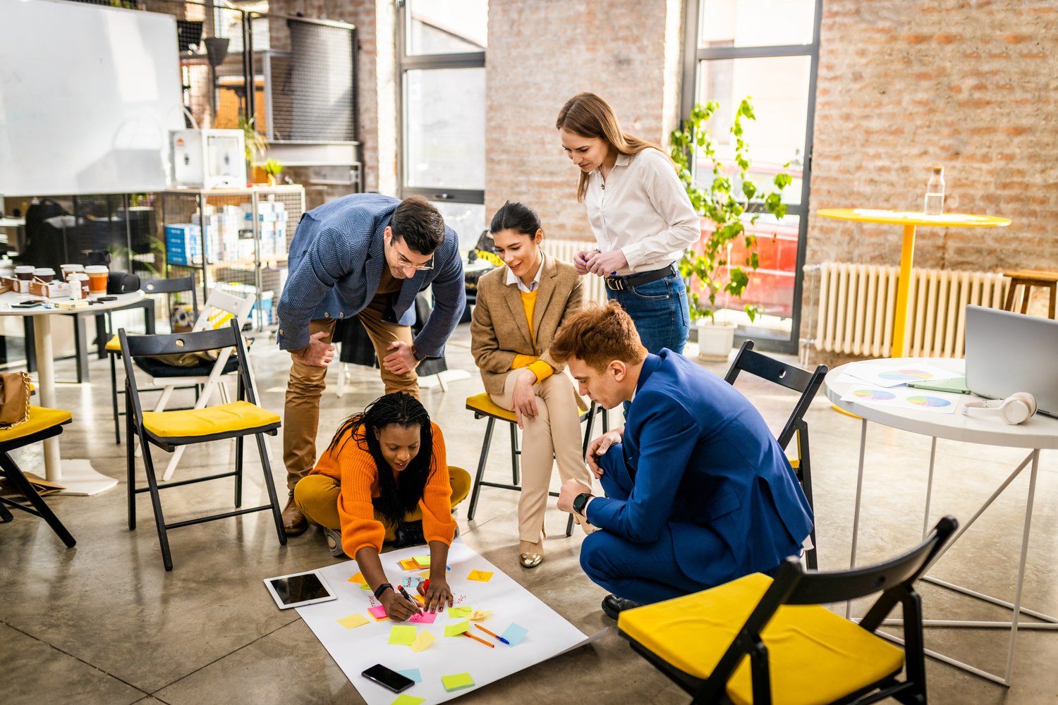 Team of five gathered around a large sheet on the floor, placing sticky notes while brainstorming