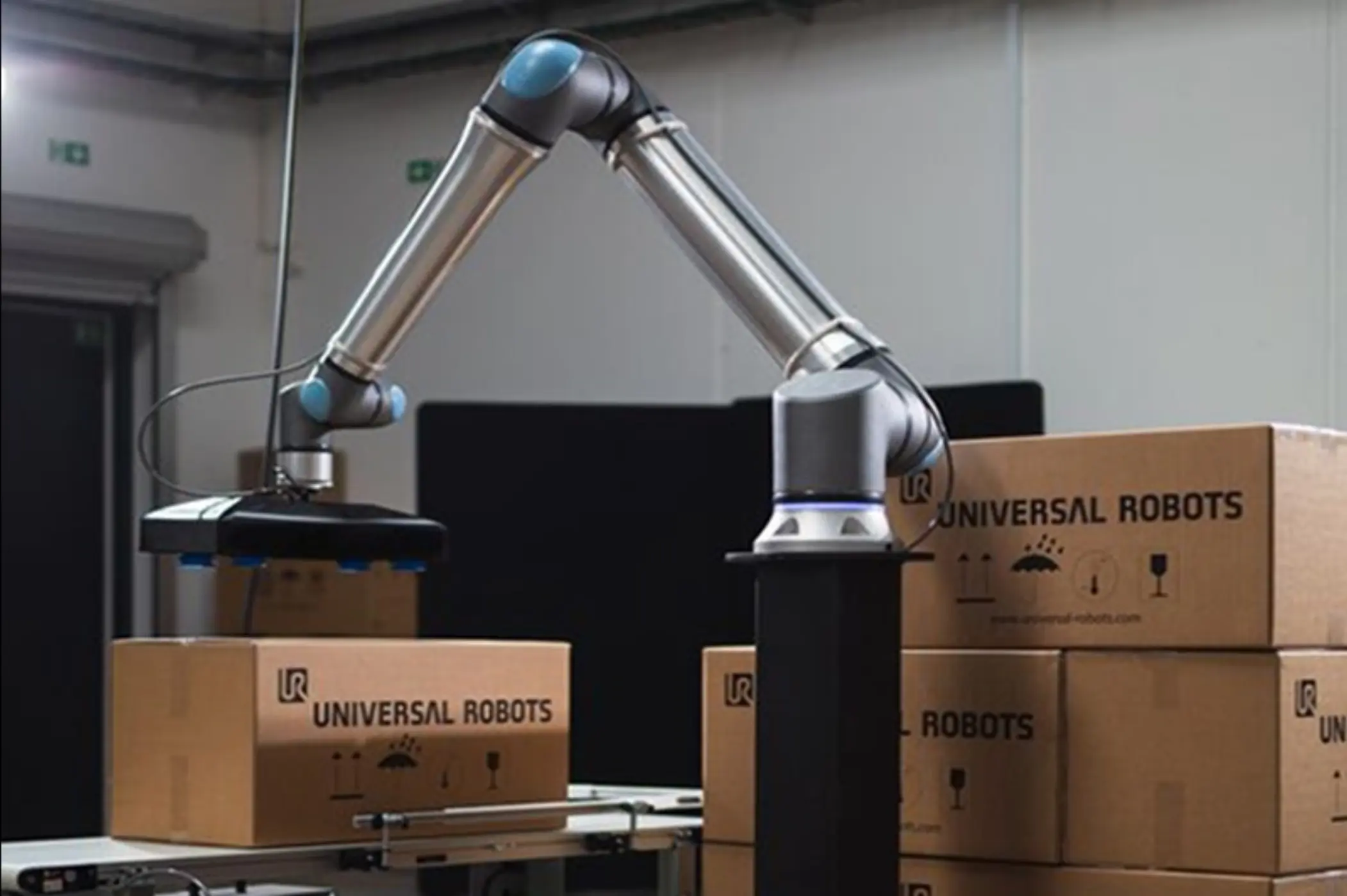 Industriell robotarm pakker esker merket Universal Robots på et samlebånd.