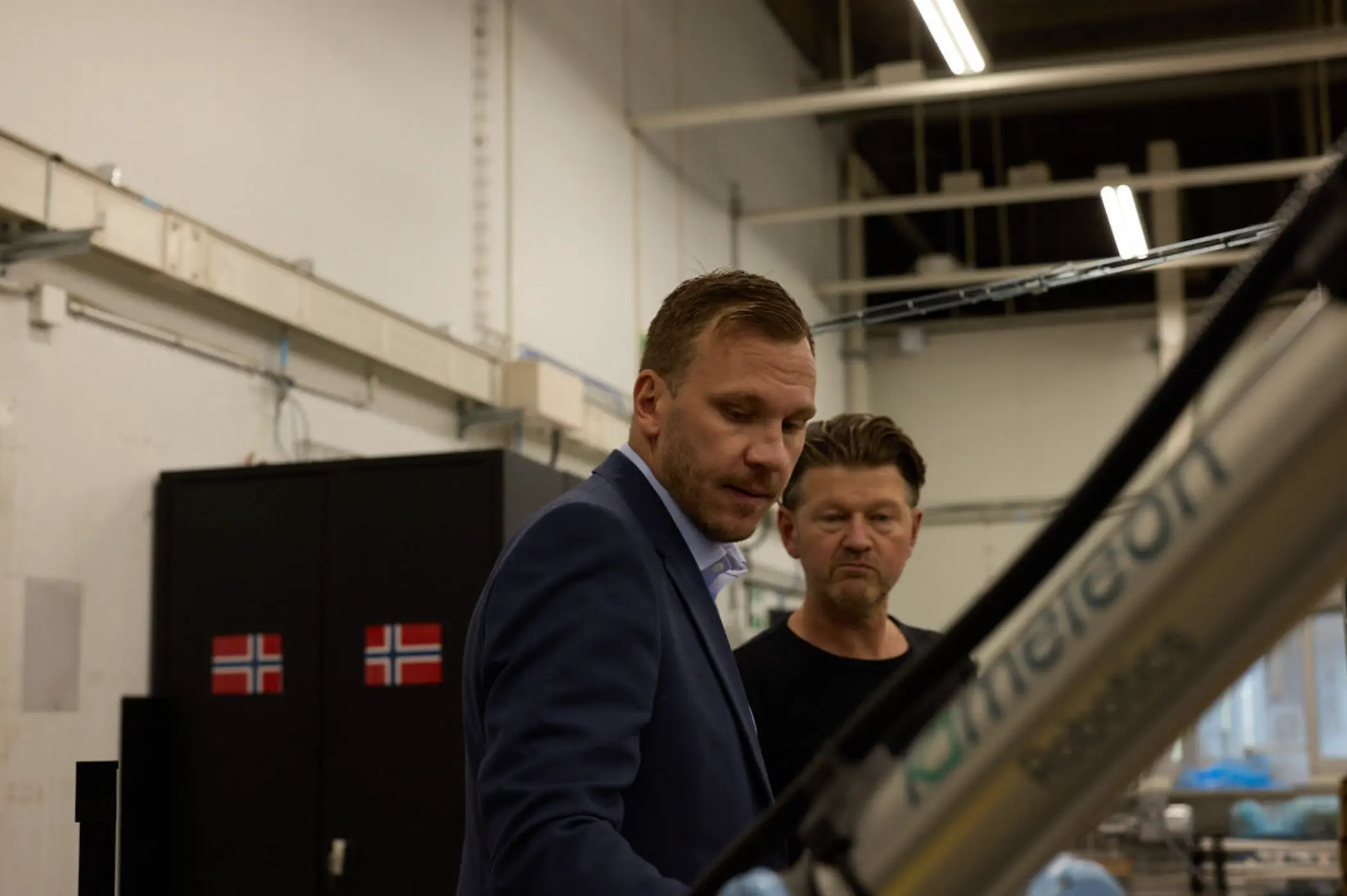 To menn i en fabrikk som ser på en maskin med teksten 'Kimatecort Robotics'.