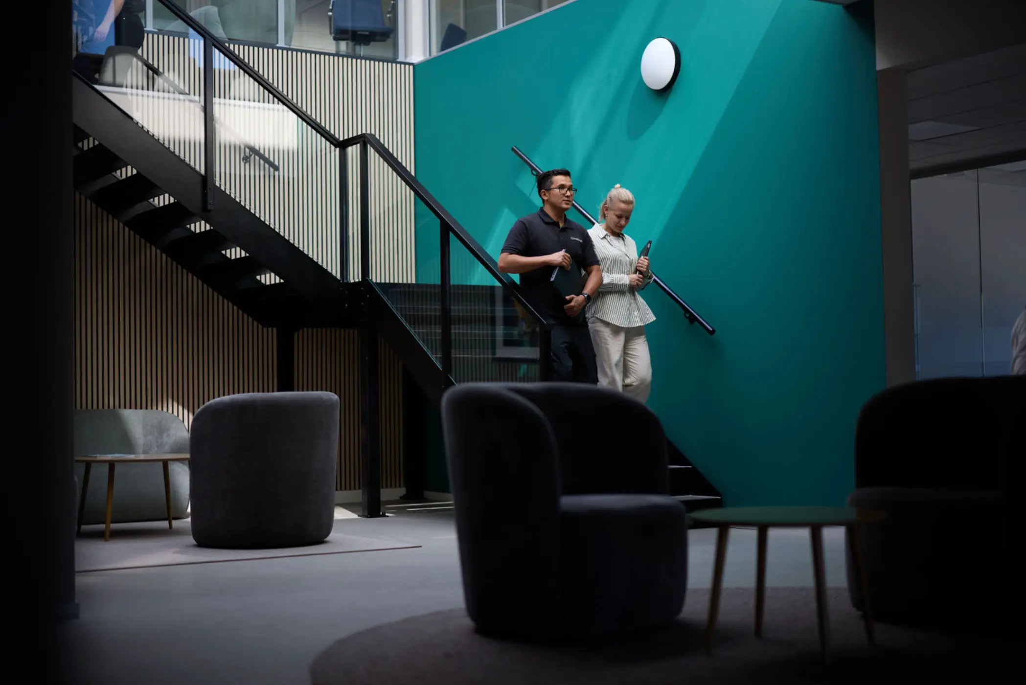 To personer går ned en innendørs trapp med turkise vegger i et moderne kontorlokale.