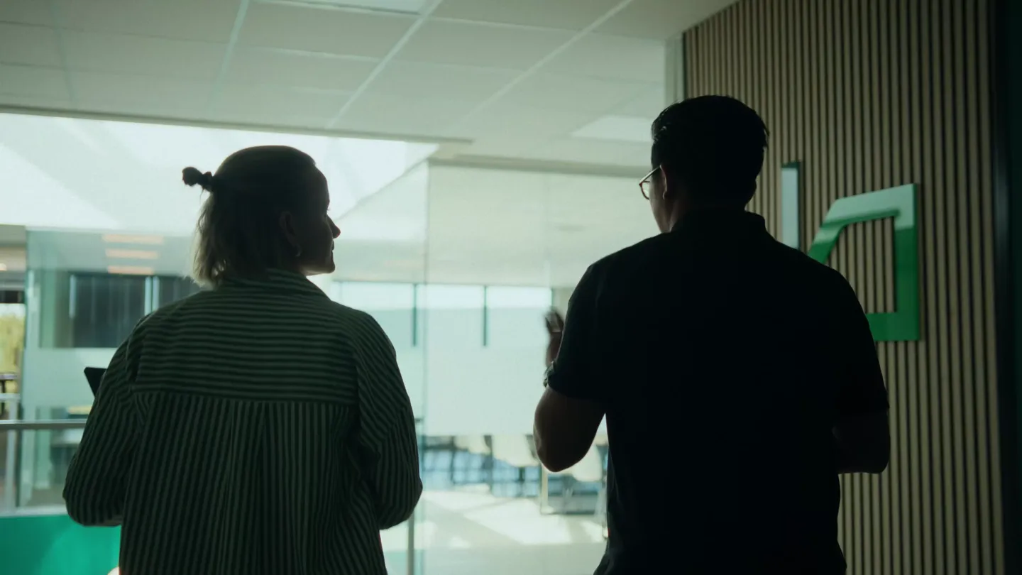 To personer i samtale sett bakfra i et lyst kontormiljø med glassvegger.