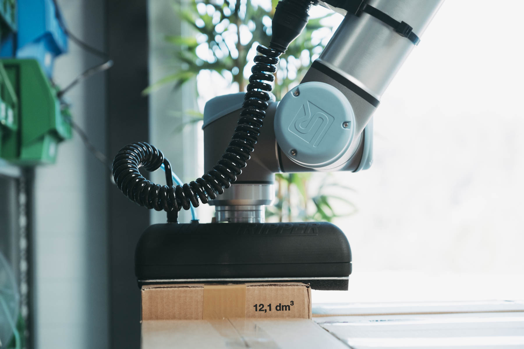 Roboterarm med vakuumgriper løfter en pappeske.