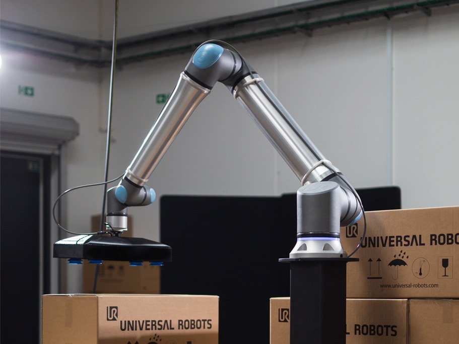 Industriell robotarm som løfter esker merket Universal Robots i et lager.