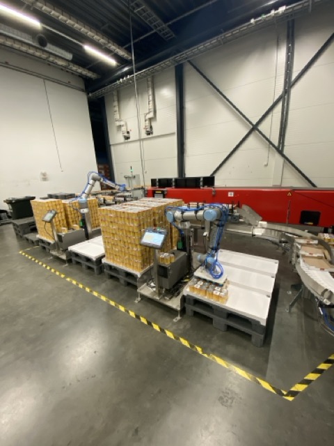 Industrirobotar pakker esker med produkter på paller i et lager med betonggulv.