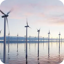 Offshore wind turbines standing in calm water at sunset with a cloudy sky.