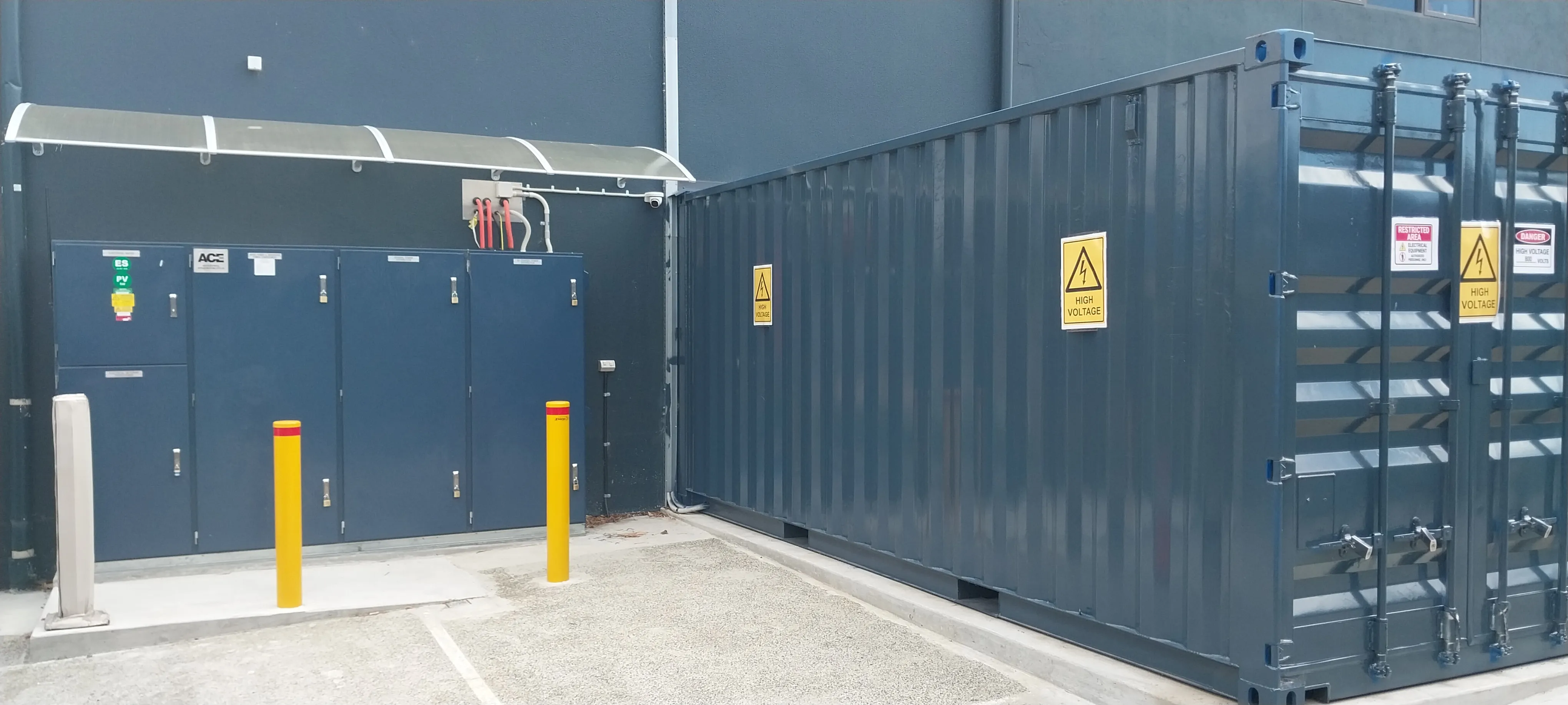 Outdoor electrical equipment room and container with multiple high voltage warning signs on walls and doors.