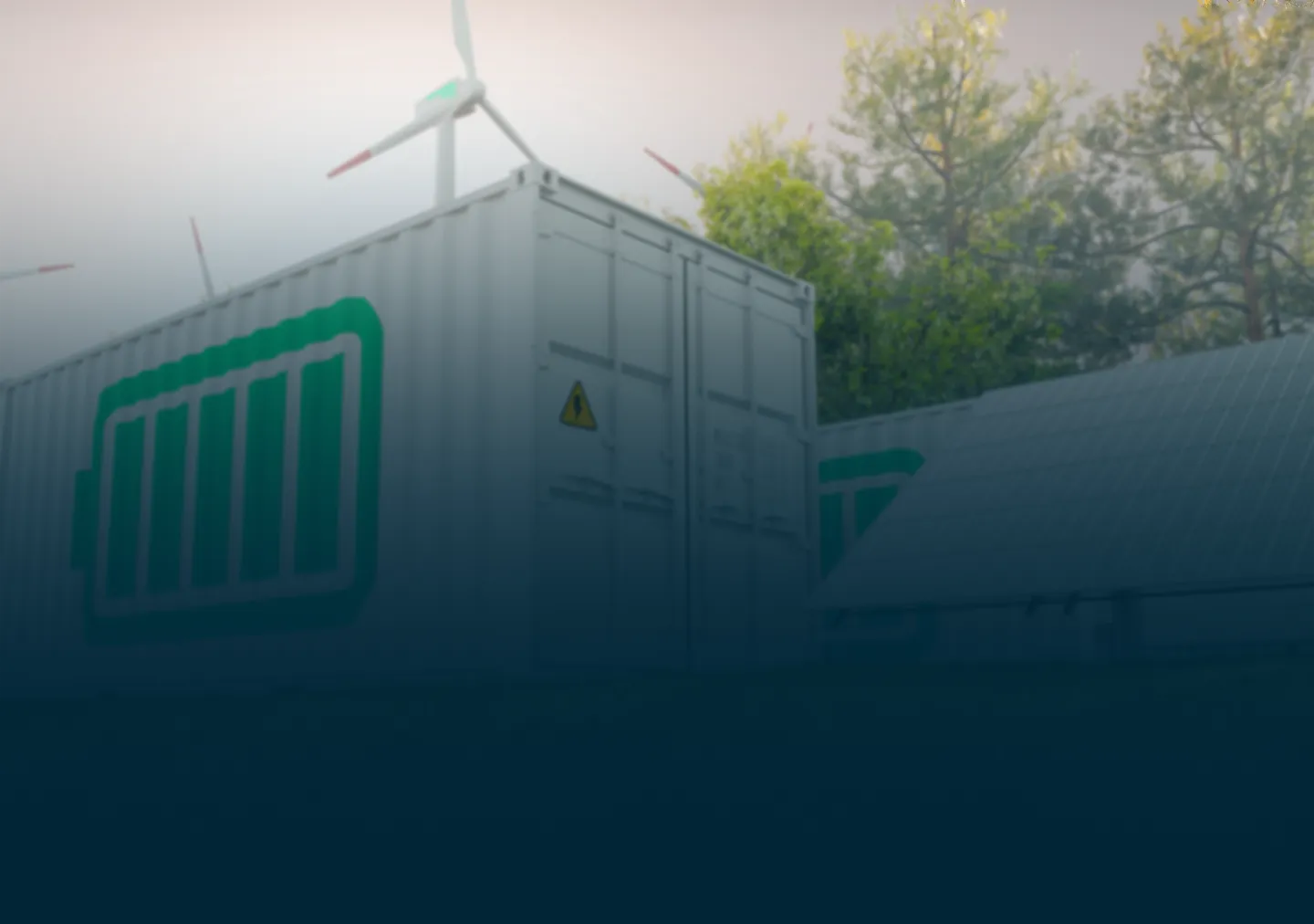 Energy storage containers near solar panels and wind turbines in a green, wooded area.