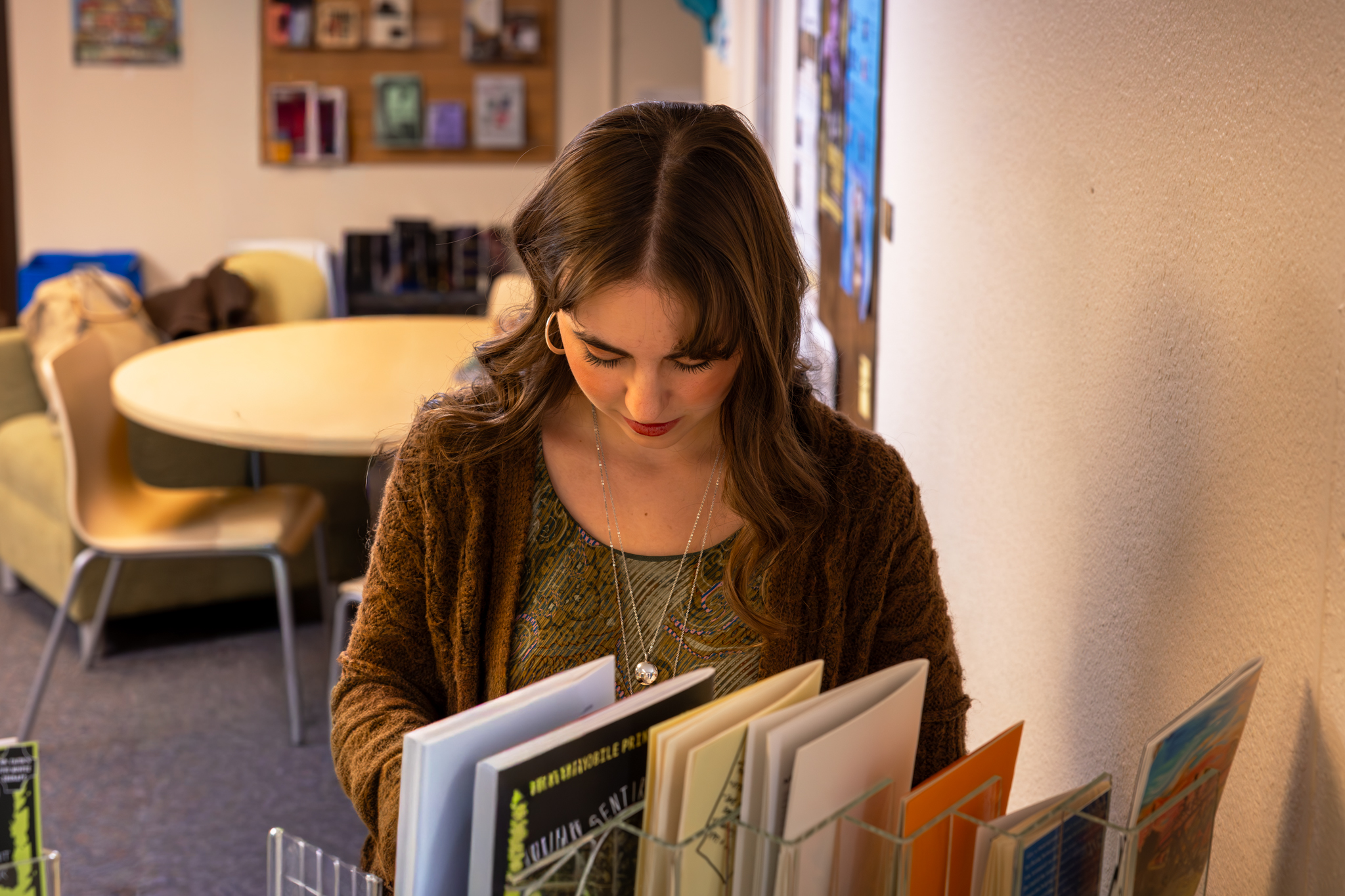 Young woman with brown hair looking down at books in a library or reading room.