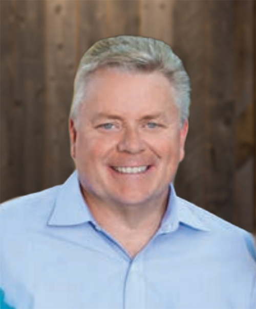 Smiling middle-aged man with light hair wearing a light blue collared shirt against a wooden background.