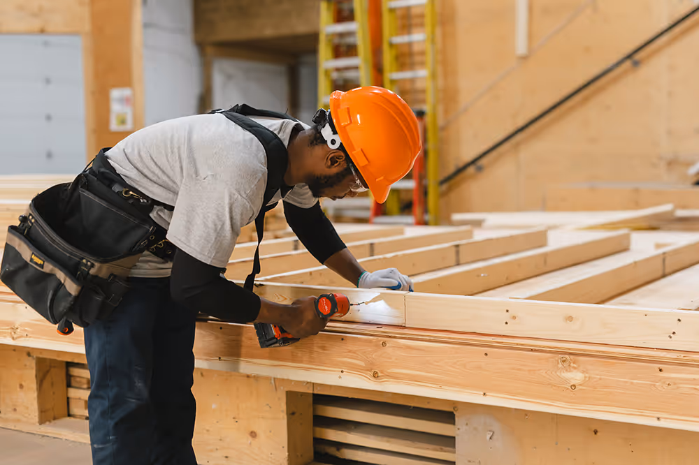 Pathways student in hard hat and toolbelt while drilling into a wooden frame