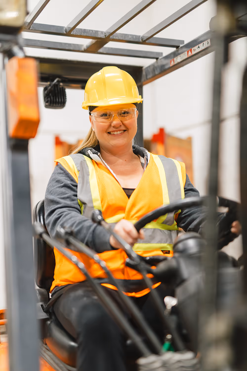 Smiling employee in hard hat and hi-vis safety vest operating a forklift