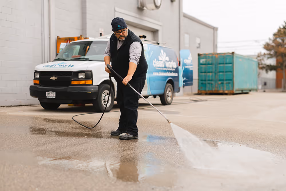Cleanworks employee using pressure washer to clean pavement outside warehouse