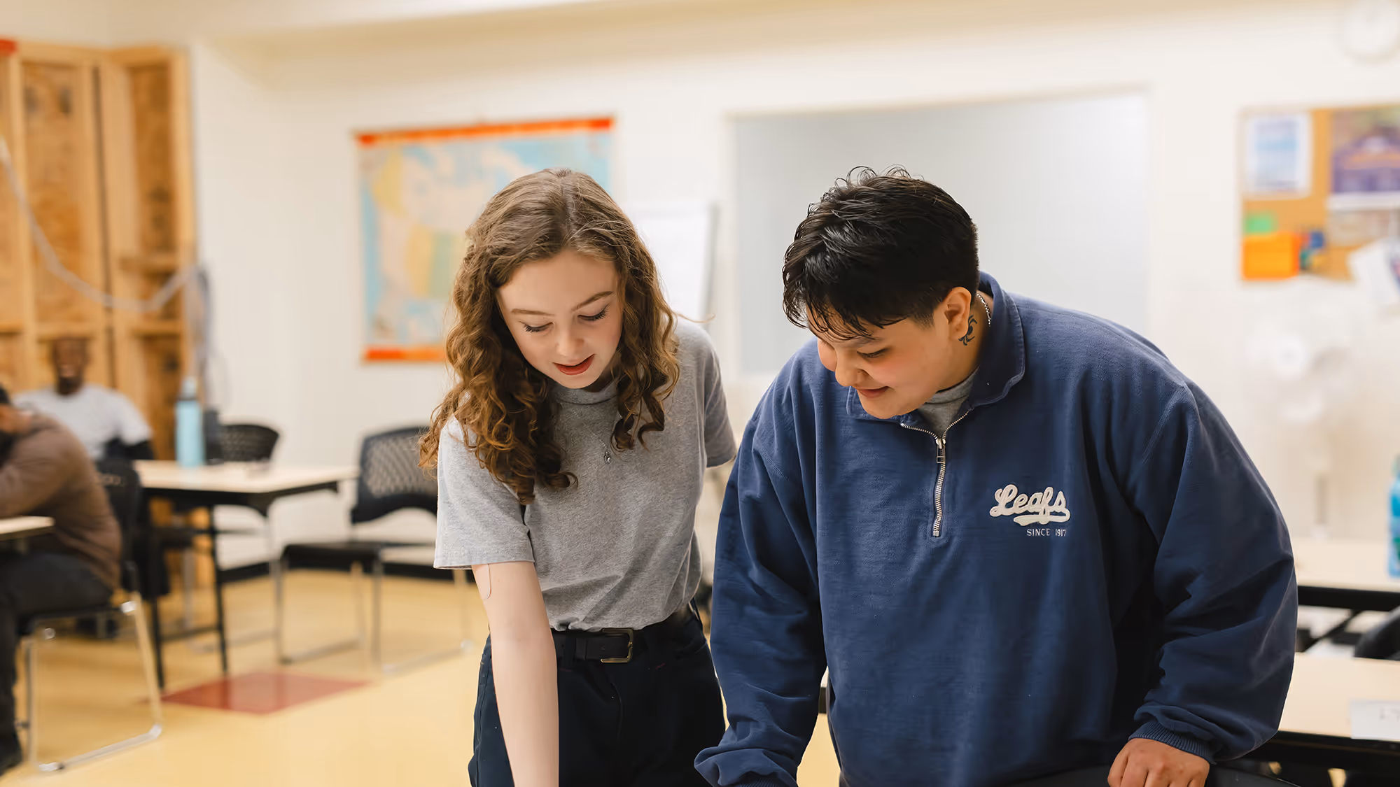 Two Pathways students standing together in classroom, smiling and looking at a document together