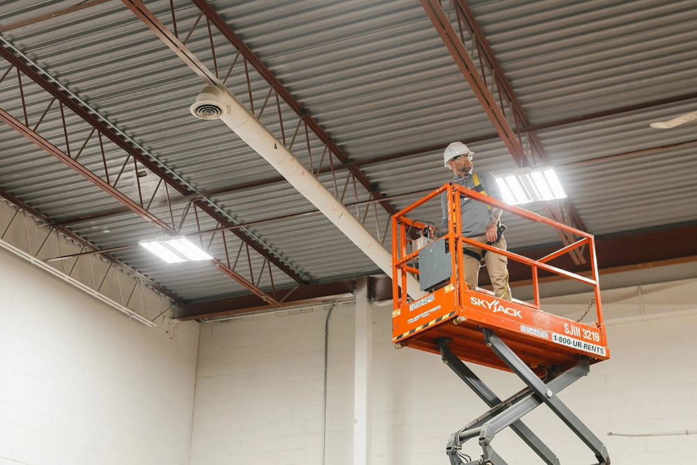Pathways Elevated Work Platform Operator certification participant standing on scissor lift extended to ceiling in warehouse
