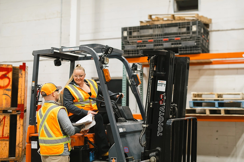 Two Pathways forklift certification participants working together. One operates the forklift while the other is looking on.