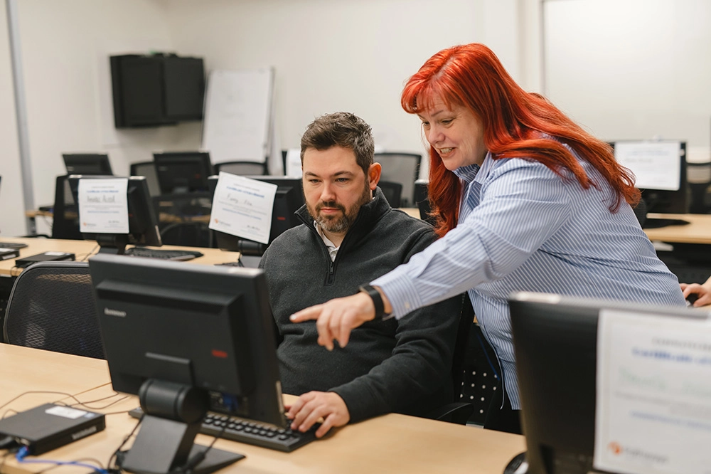 Pathways staff member pointing at computer screen in front of Pathways Skills Training participant in classroom