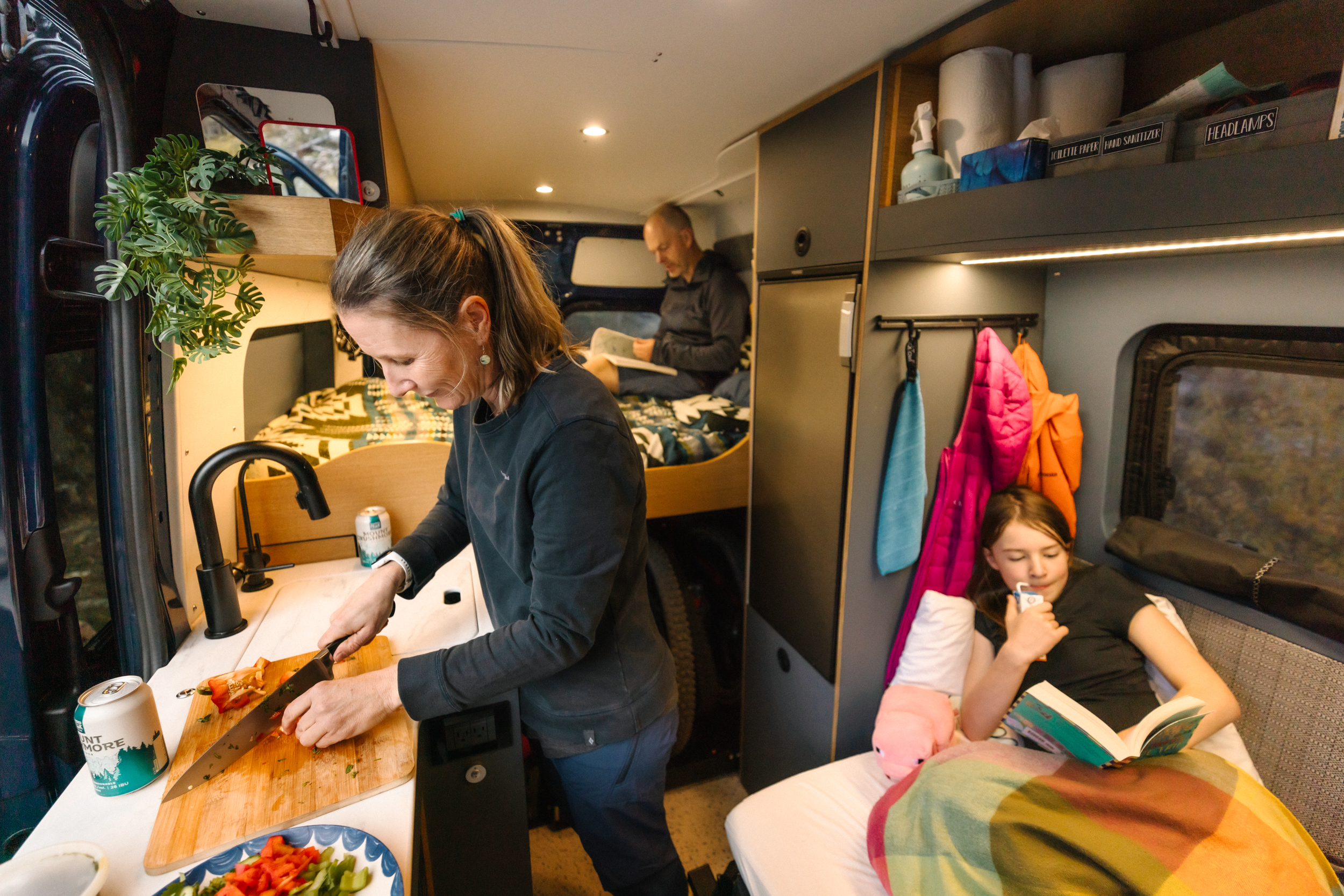 Nathalie cooking in the kitchen of the family's Yama Teton01N while Keira reads on her seat-bed and Frank relaxes in the back