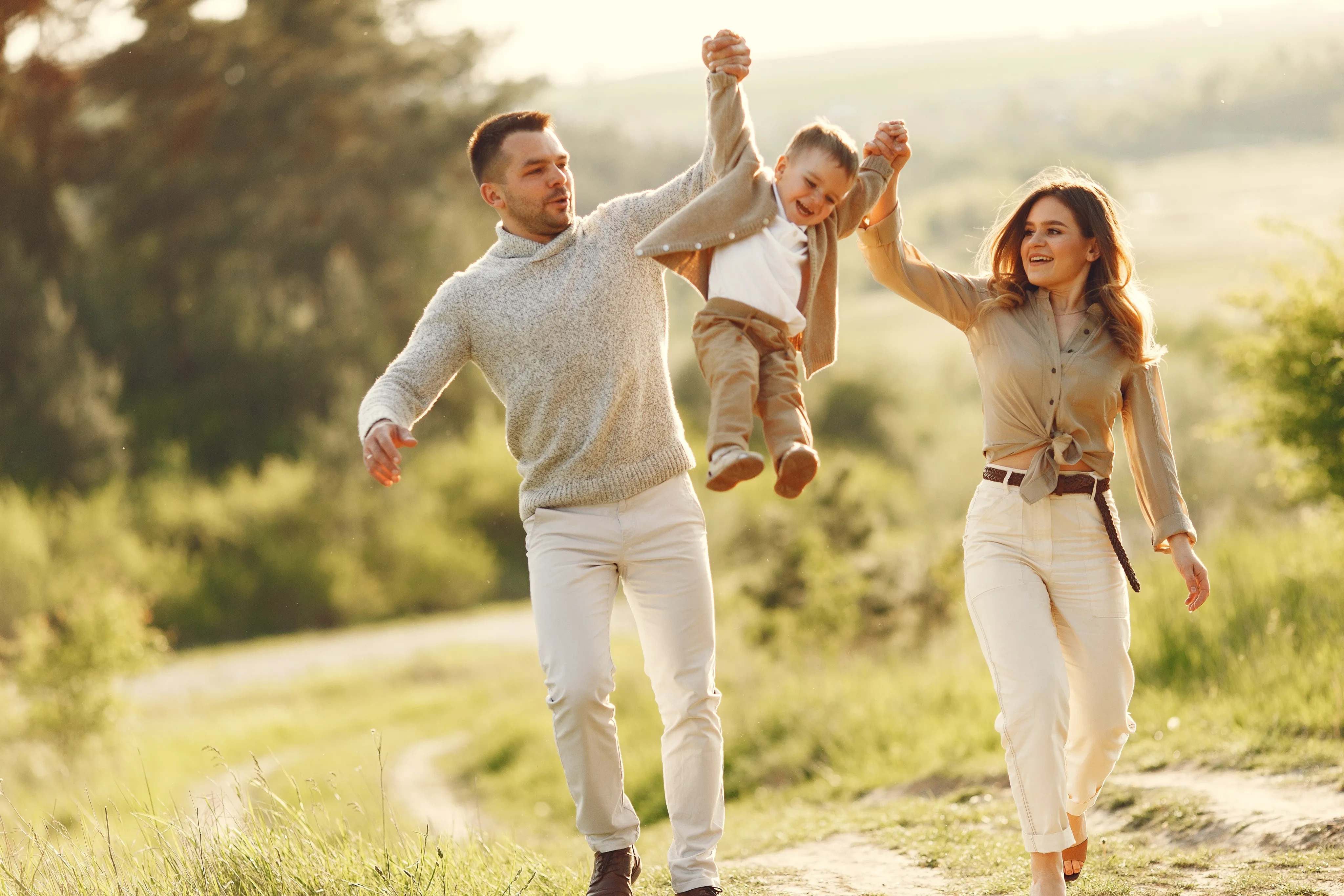 Smiling parents swinging their child in a green park, insured by an independent insurance agency in South Florida.