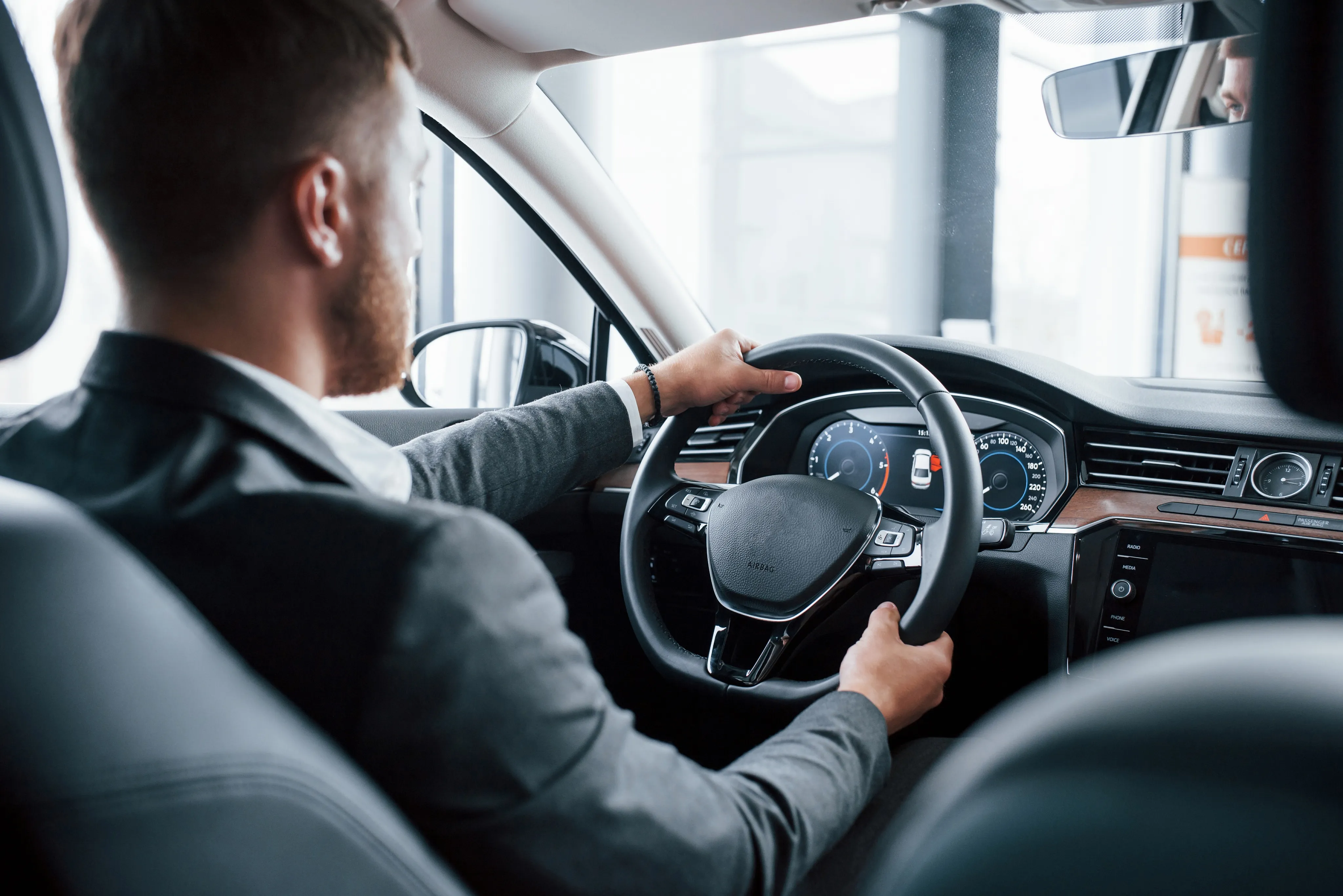 A professional man in a suit confidently grips the steering wheel of his modern vehicle, representing the business-class service and expert support available from an independent insurance agency in South Florida.