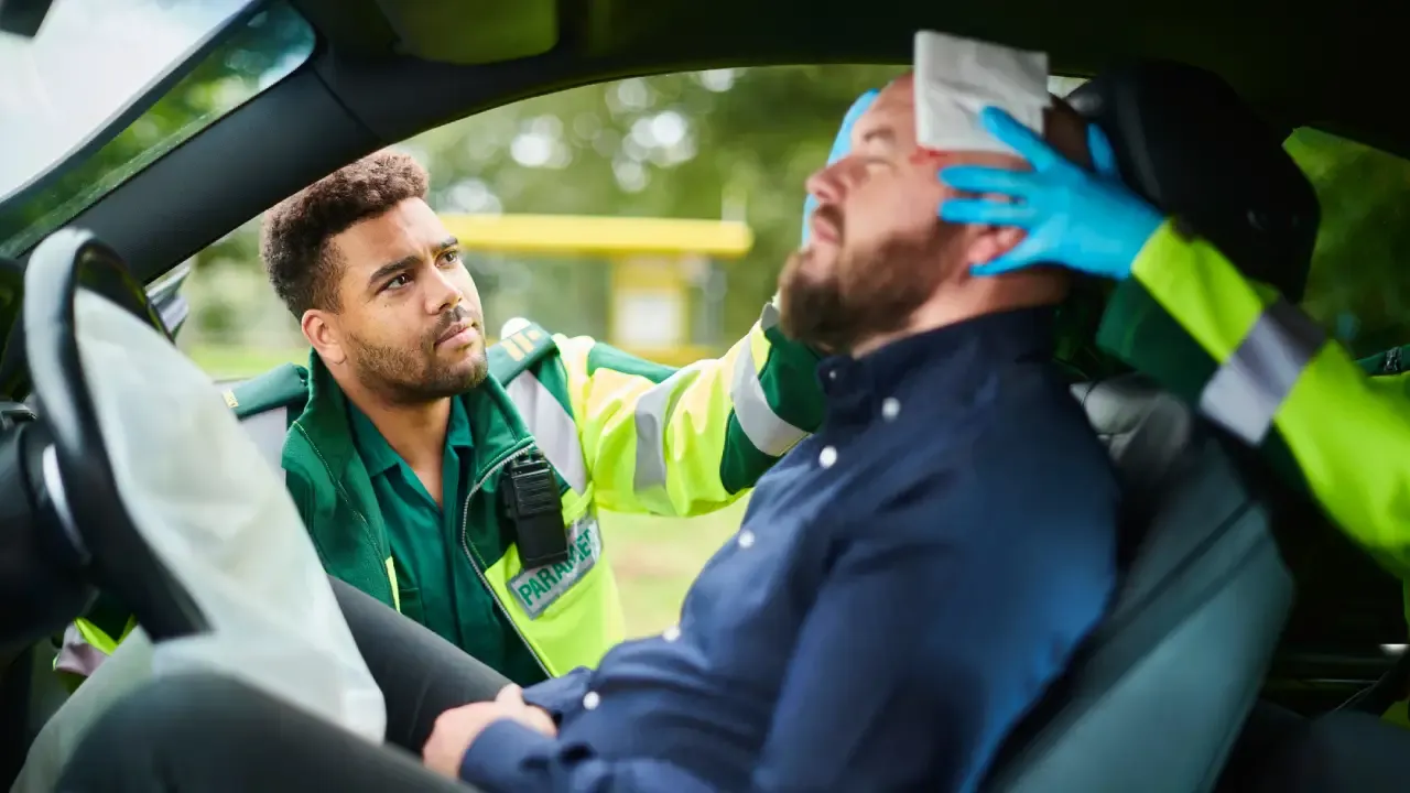 A paramedic in gloves assists an injured man in the driver's seat after a crash, highlighting the emergency support offered by an independent insurance agency in South Florida during medical situations.