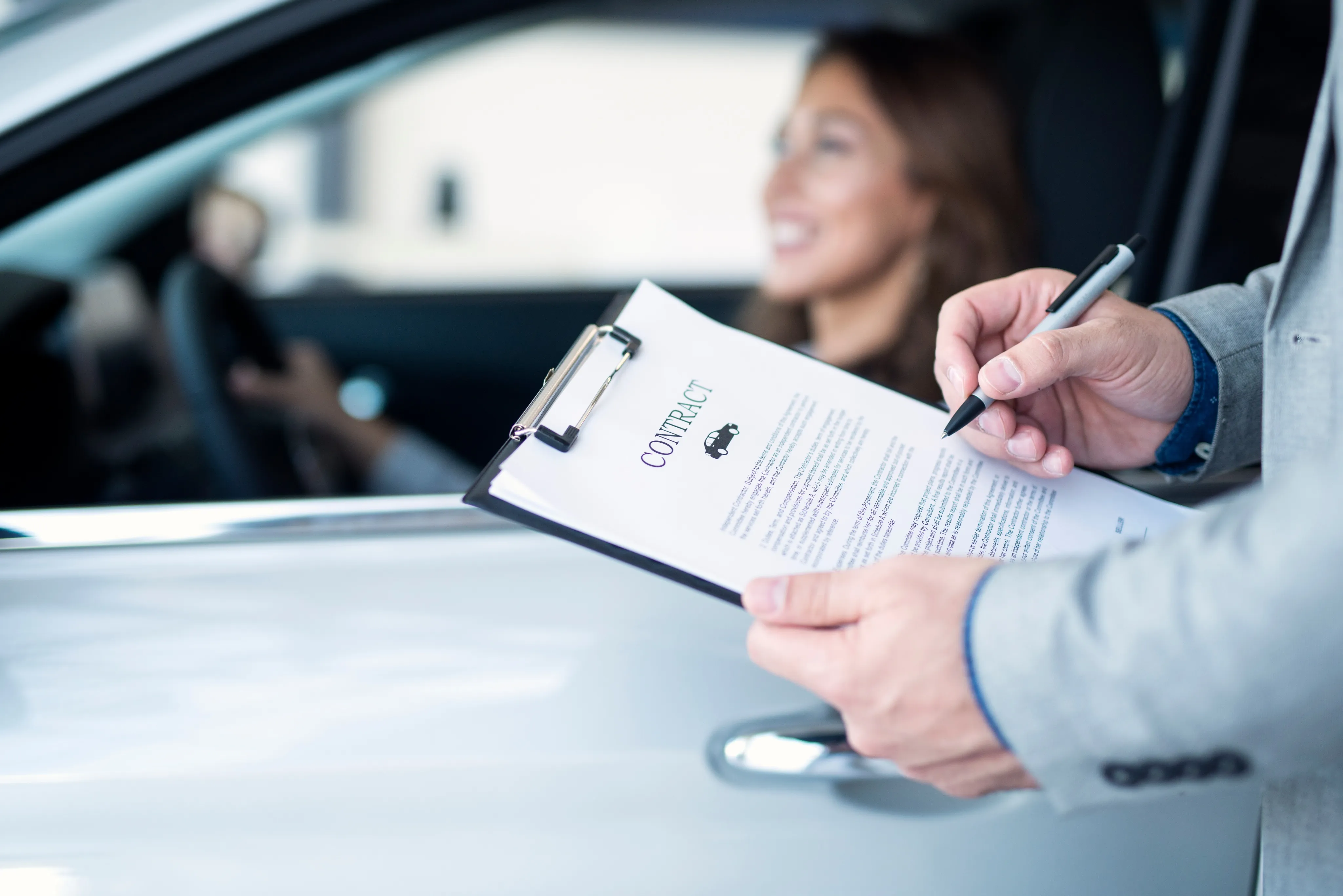 Person signing a car document while a woman smiles in the driver's seat in South Florida.