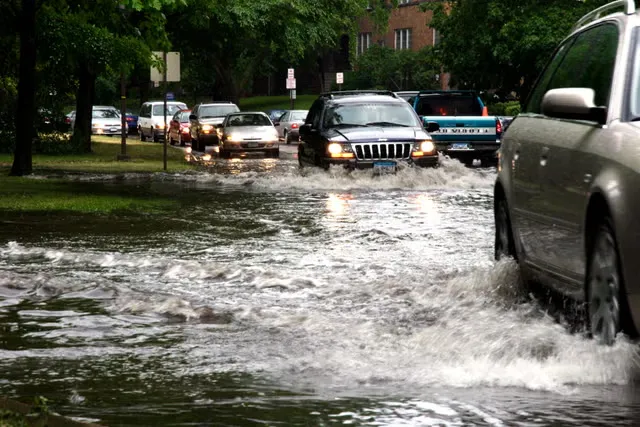 Cars navigate a flooded street in South Florida, traffic lining up behind small business vans.
