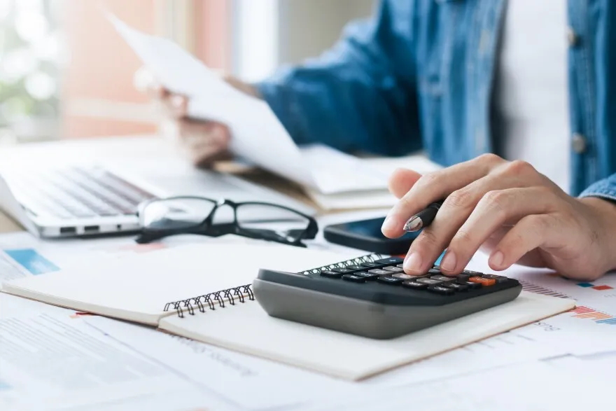 Person calculating with papers, notebook, and glasses—reviewing business property insurance.