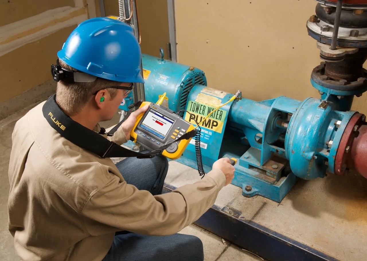 A worker in safety gear inspects a blue water pump, vital business property.