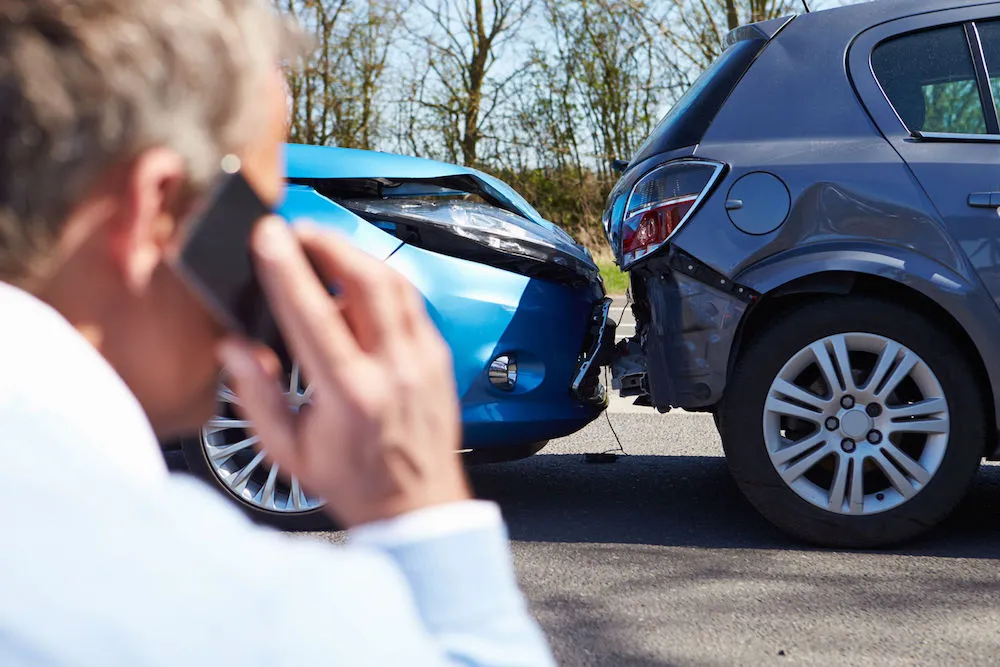 A man on the phone near two cars after a rear-end collision, highlighting general liability coverage.