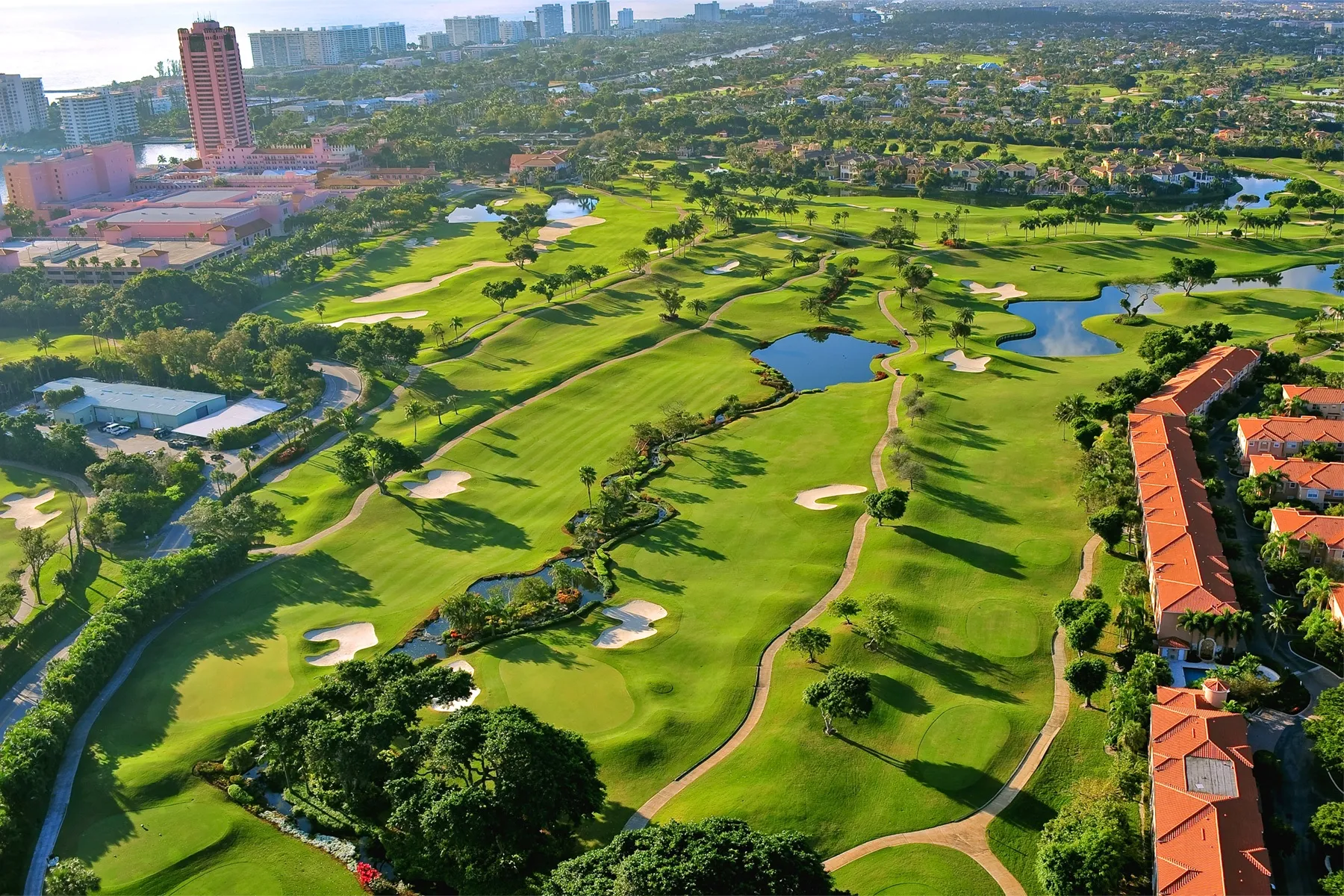 Aerial view of a scenic Coral Springs golf course with lush greens, water features, and nearby commercial buildings.
