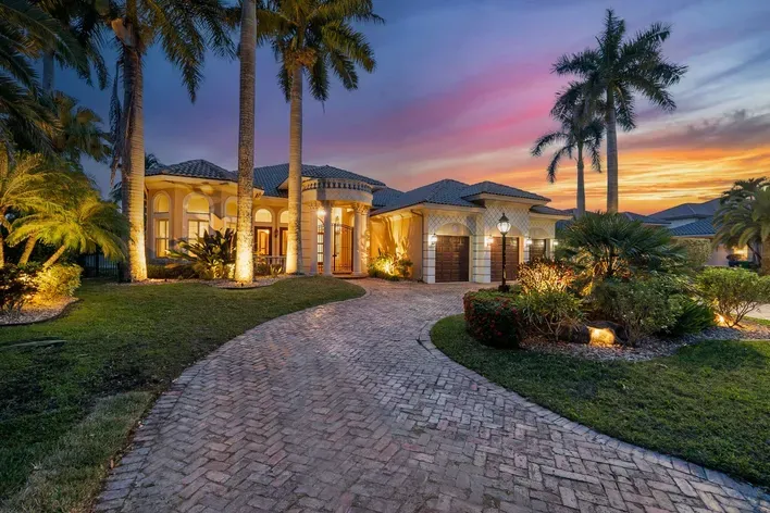 Luxurious Coral Springs home with palm trees and brick driveway at sunset, ideal for homeowners’ insurance.