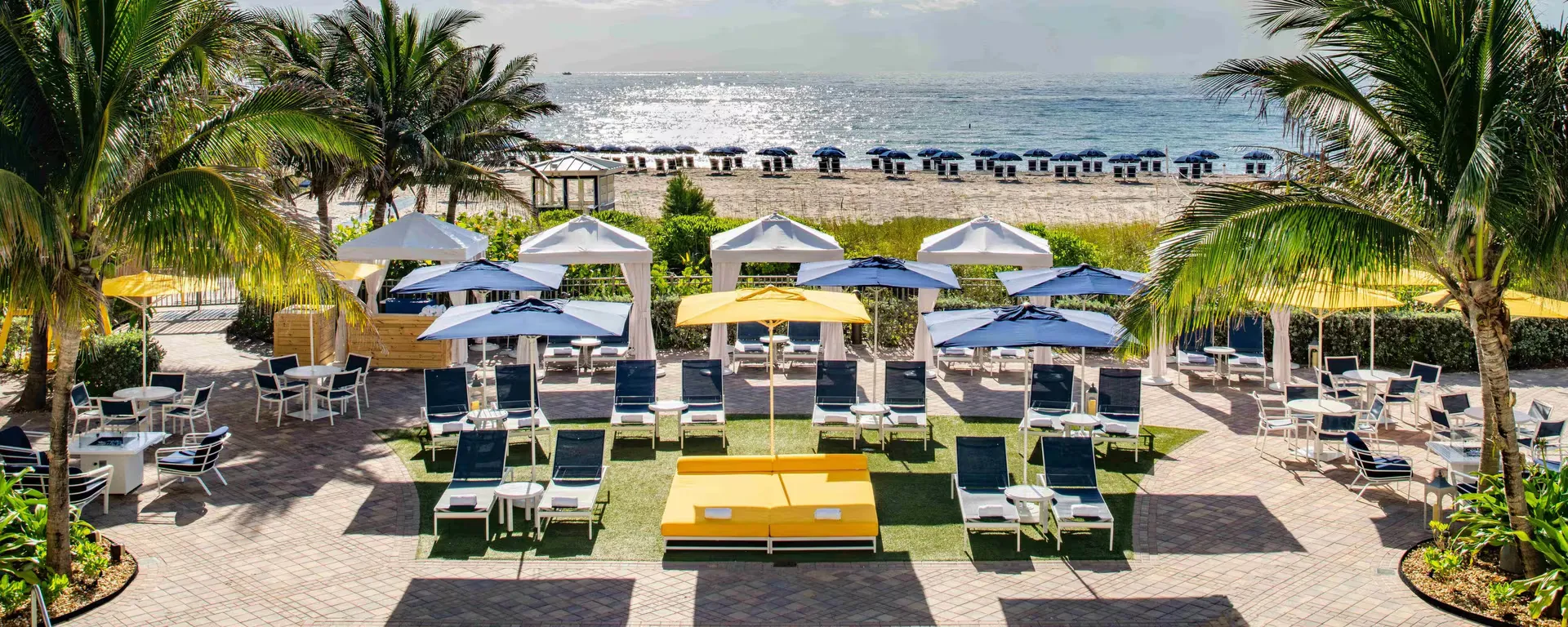 Resort-style beach setup in Pompano Beach, Florida with lounge chairs, cabanas, and umbrellas by the ocean.