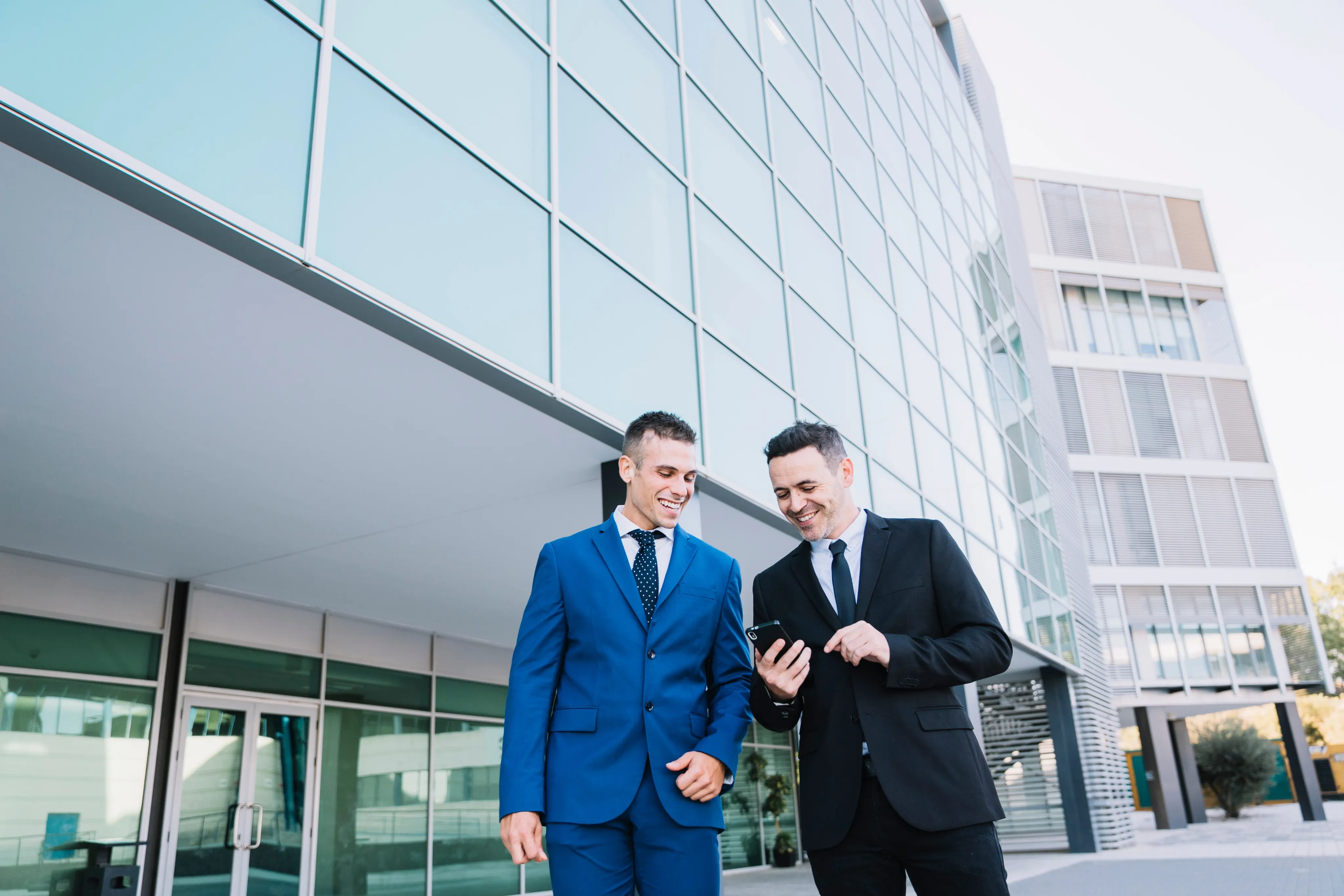 Two business professionals in suits stand outside a modern office building in Pompano Beach, discussing insurance.