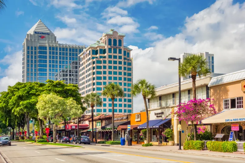 Downtown Fort Lauderdale street view with palm trees, shops, and high-rise office buildings under a sunny sky.