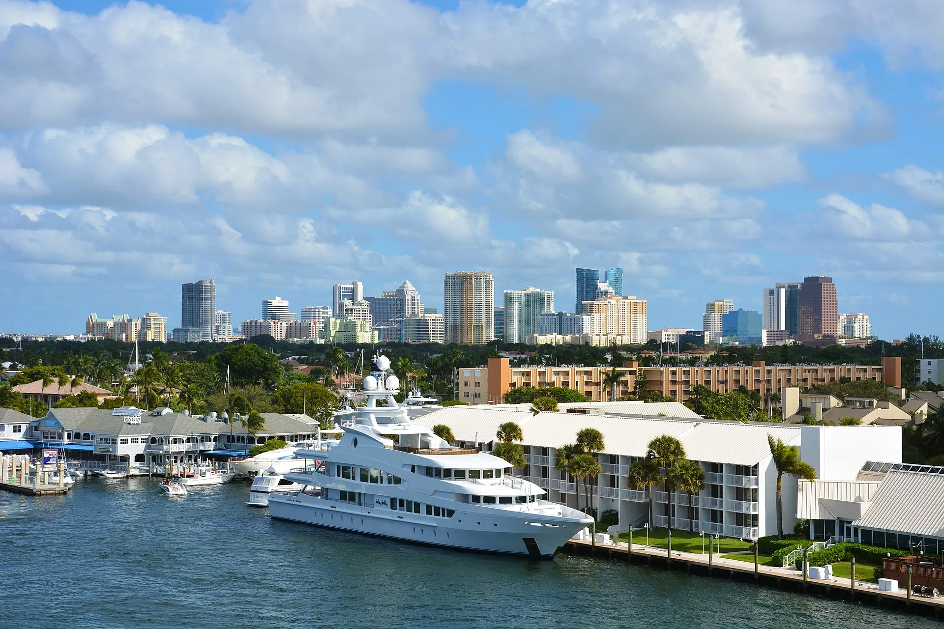 Luxury yachts docked on the water with the Fort Lauderdale skyline in the background under a partly cloudy sky.