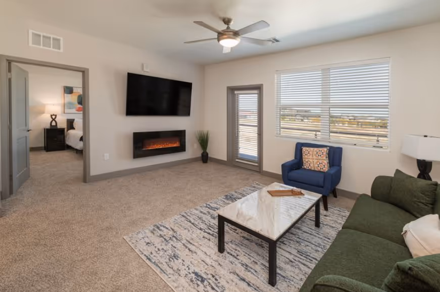 Spacious open-concept living area and kitchen with wood-look flooring and a modern wall-mounted fireplace at Pueblo Springs in Pueblo West, CO.