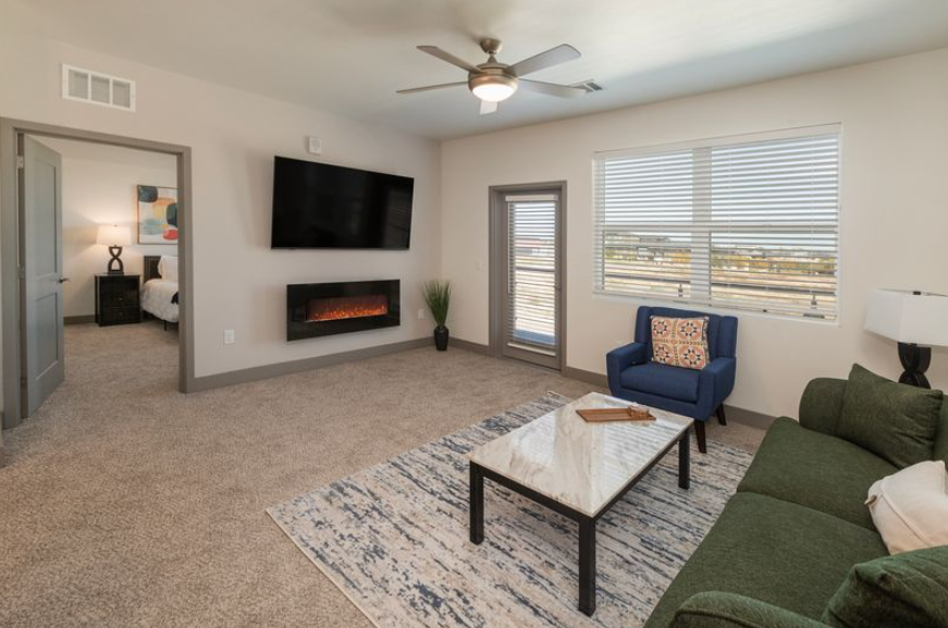 Spacious open-concept living area and kitchen with wood-look flooring and a modern wall-mounted fireplace at Pueblo Springs in Pueblo West, CO.