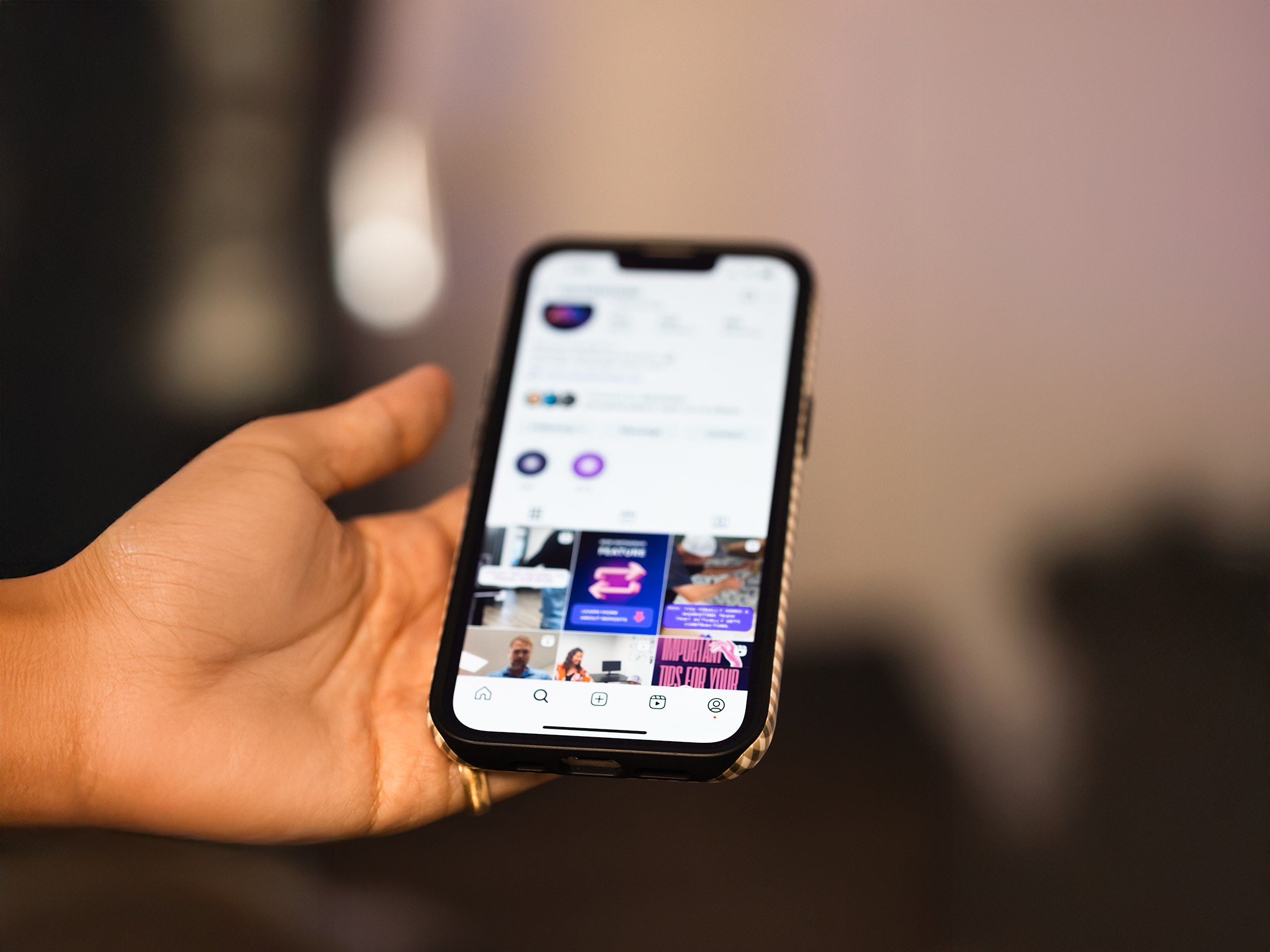 Hand holding a smartphone displaying an Instagram profile page with posts and navigation icons.