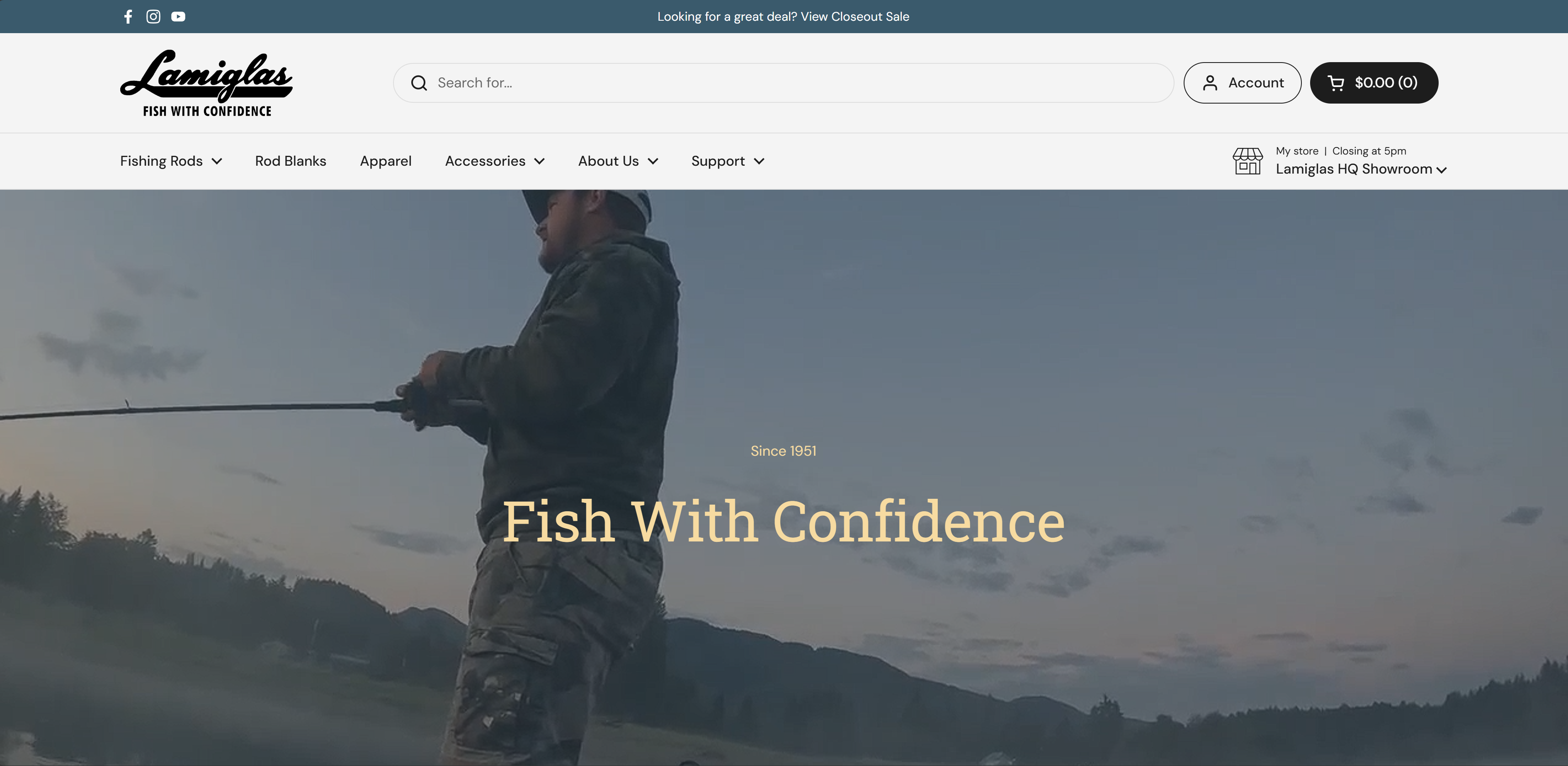 Person in camouflage clothing fishing with a rod at dusk with mountains and trees in the background.