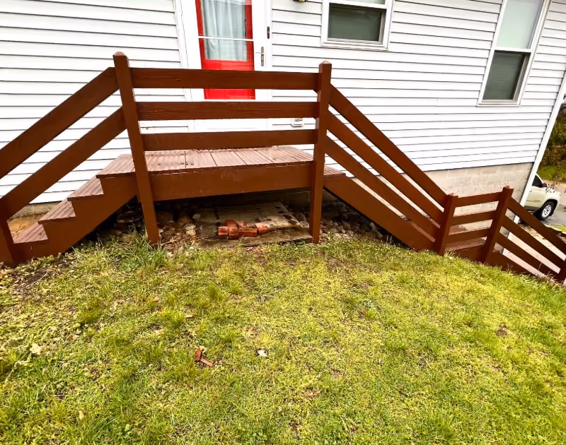 Newly installed long wooden staircase with handrails leading to front door entrance.