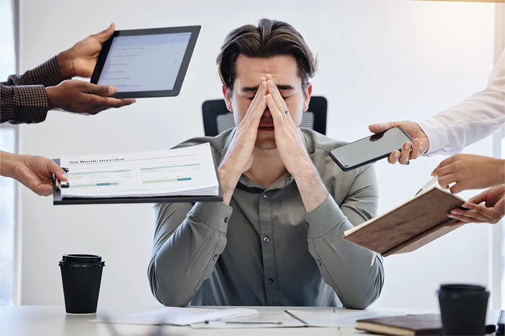 Overwhelmed business leader surrounded by reports, devices, and demands,illustrating burnout from unmanaged effort