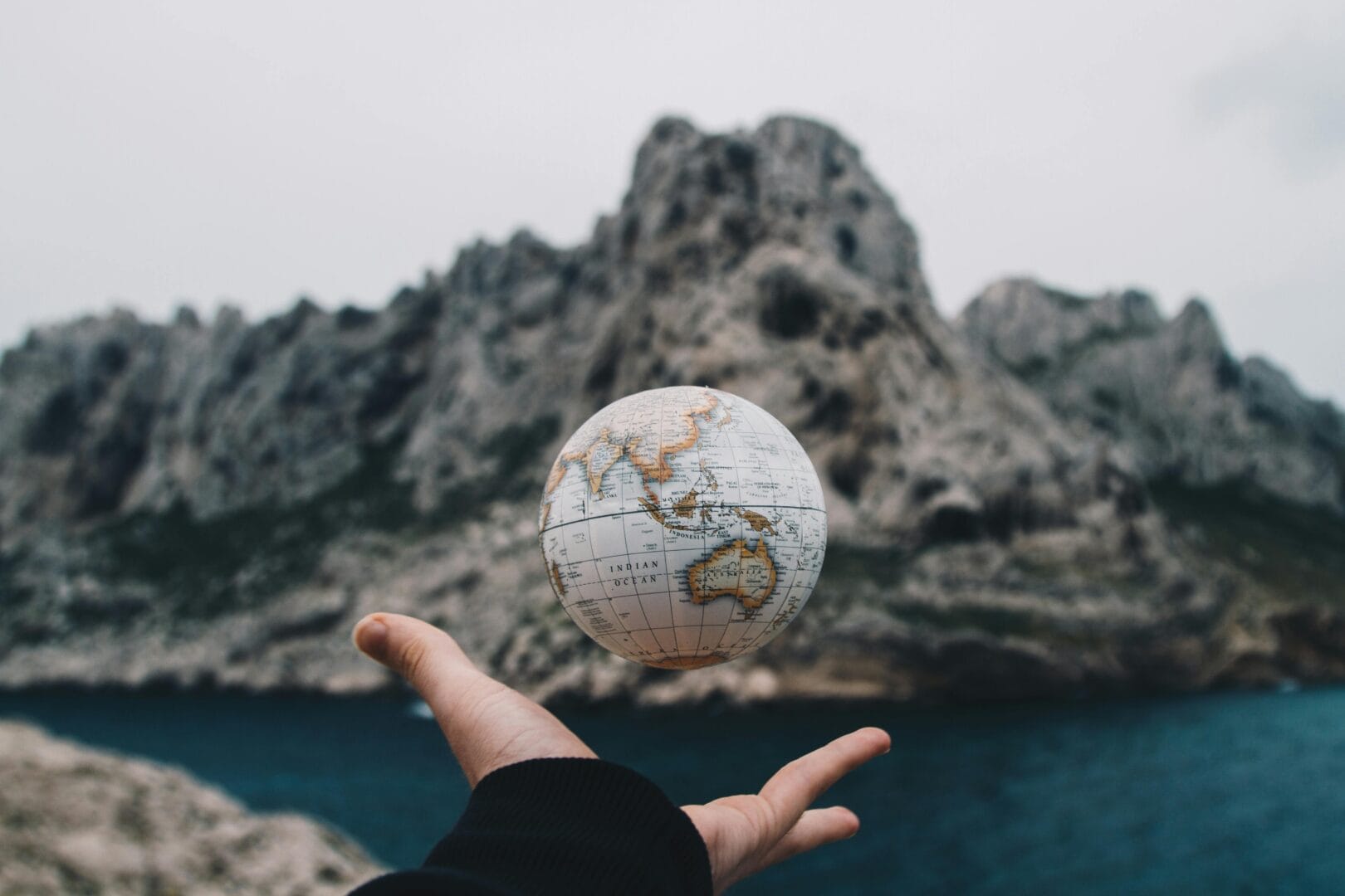 Person holding a small globe with a mountainous landscape in the background.