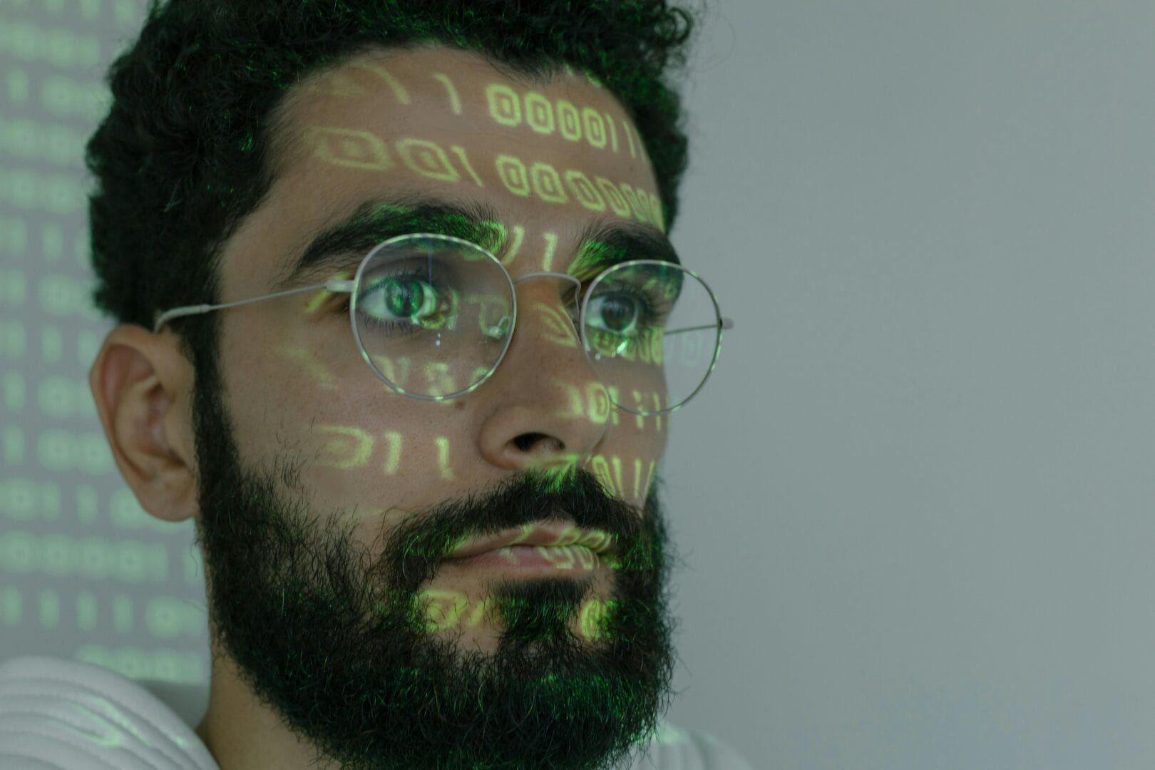 Close-up of a man with a beard and glasses, with binary code projected onto his face.