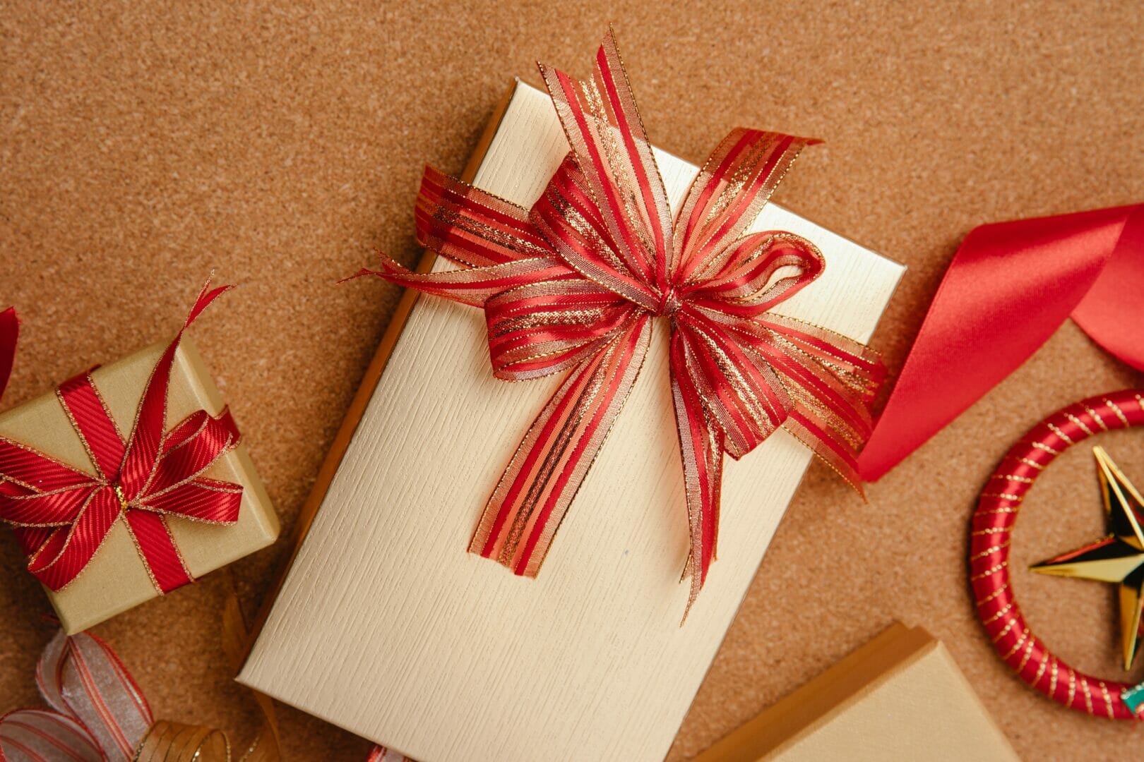 Gift wrapped in light-colored paper with a red ribbon on a brown surface.