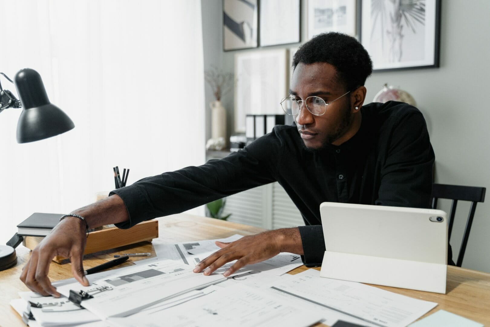 Man sitting at a desk with documents and a laptop, reaching for a pen