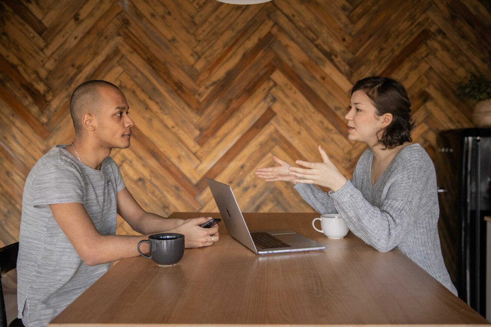 Two people having a discussion over a table with a laptop and coffee cups