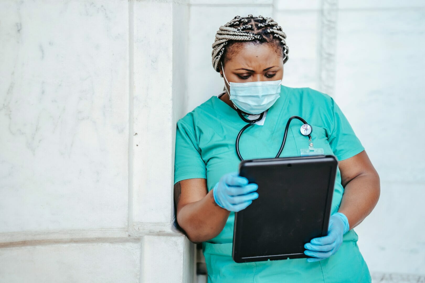 Healthcare worker in scrubs and a mask holding a tablet