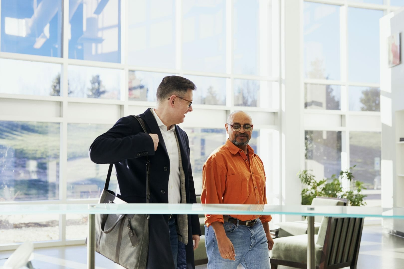 Two men walking and talking in a modern indoor setting with large windows